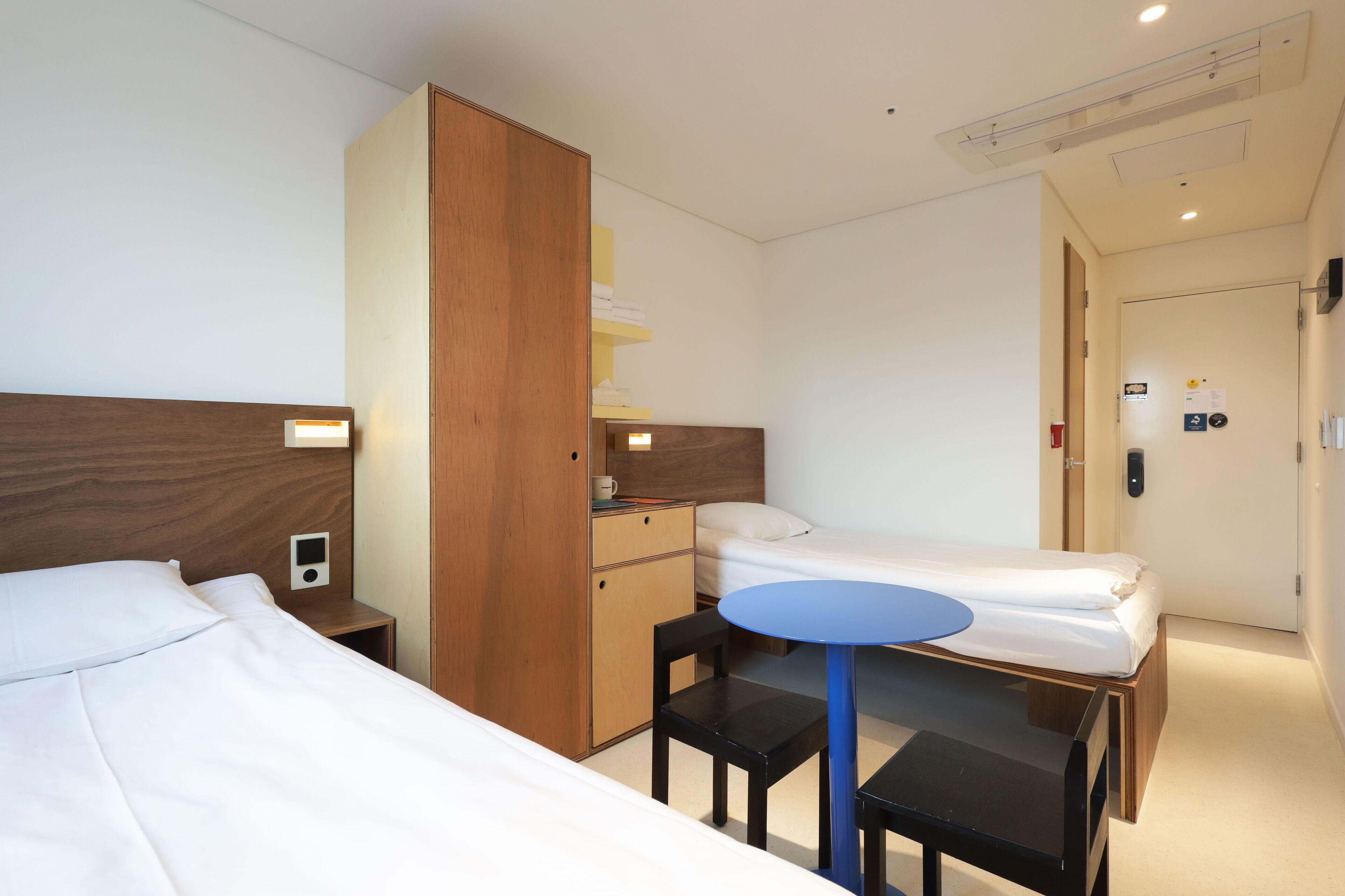 Ein Hotelzimmer mit zwei Betten, einem Schreibtisch, einem Stuhl, einem kleinen Tisch und einem Kleiderschrank.