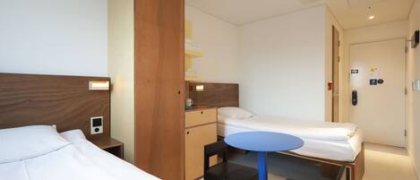 Ein Hotelzimmer mit zwei Betten, einem Schreibtisch, einem Stuhl, einem kleinen Tisch und einem Kleiderschrank.