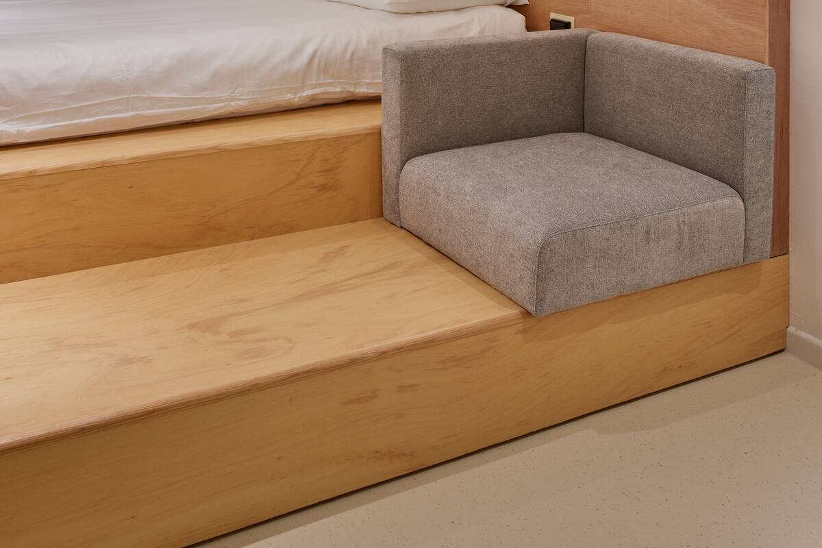 A modern bedroom with a wooden headboard, a bed with white linens, and a grey upholstered chair.