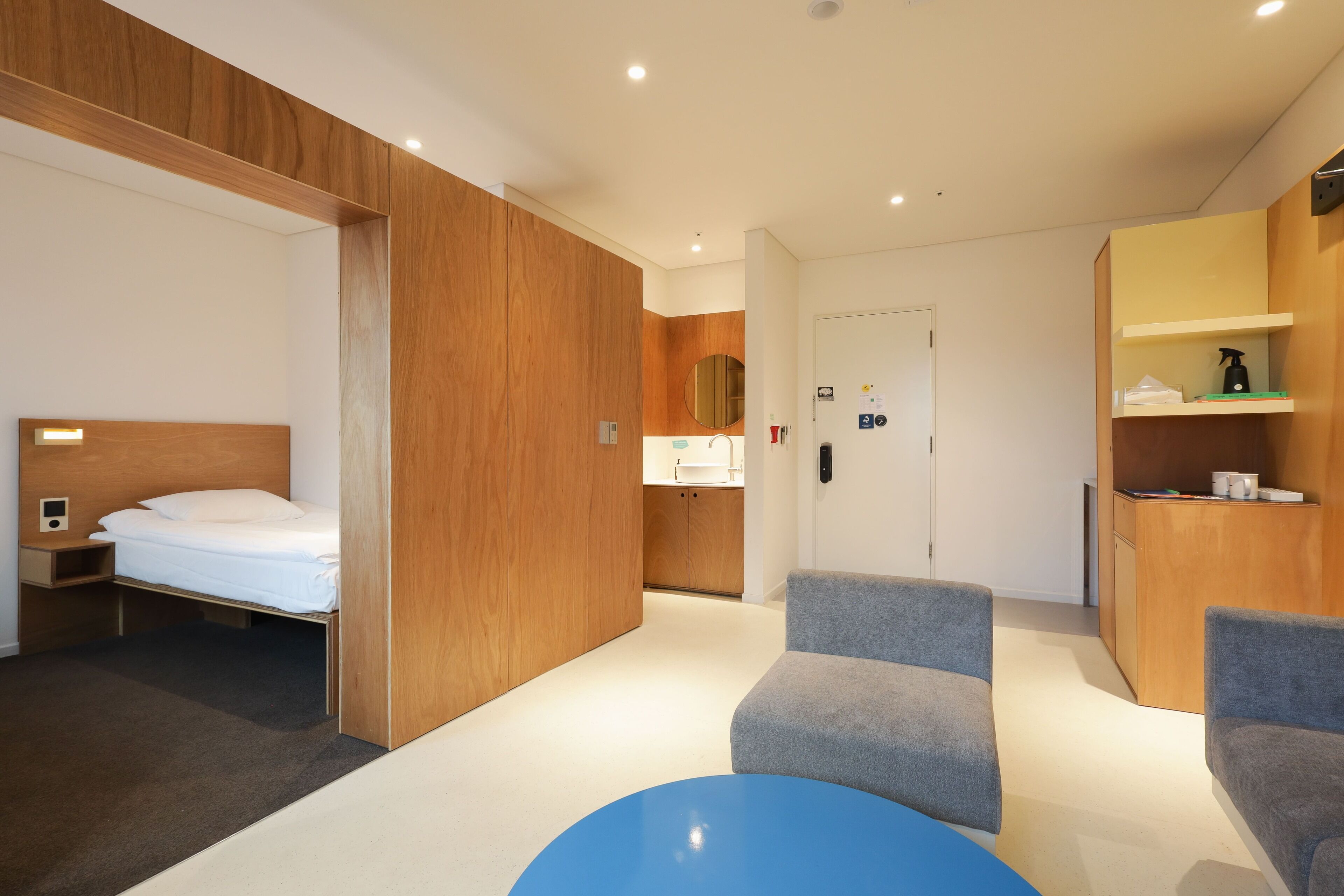 Une chambre d’hôtel moderne équipée d’un lit, d’un bureau, d’une chaise, d’une petite table et d’un coin cuisine.