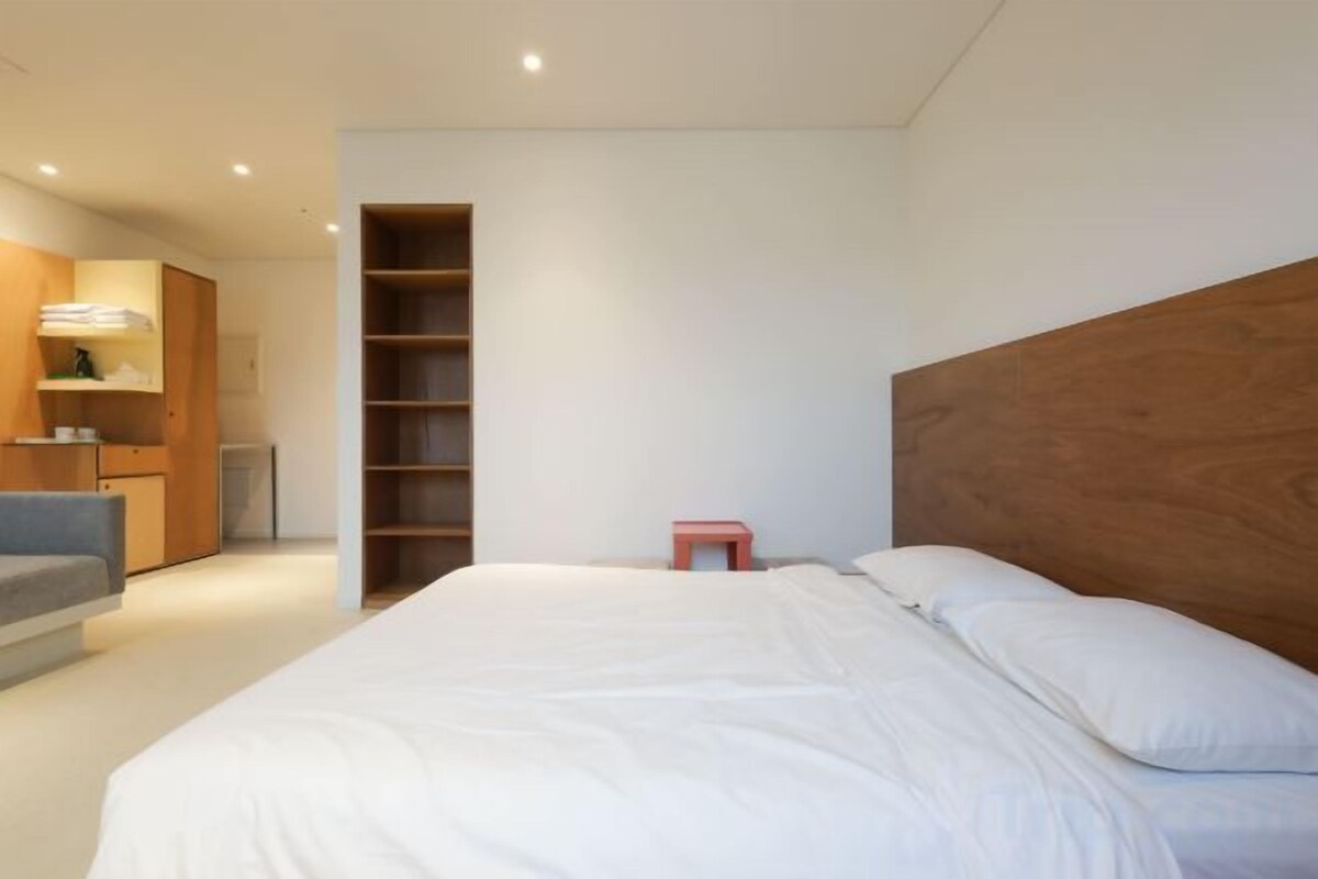 A bedroom with a large bed, a wooden headboard, a built-in wardrobe, and a small stool.