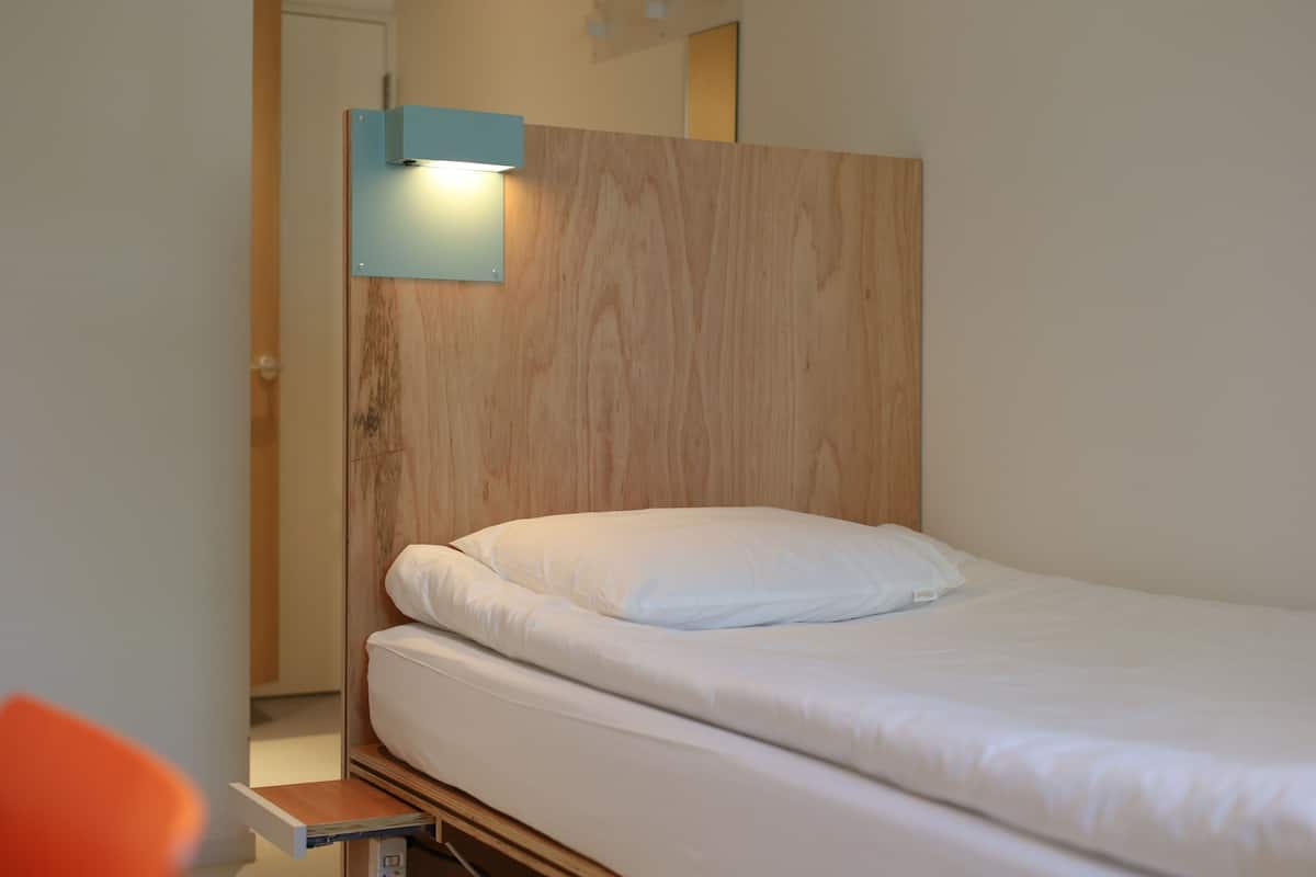 A single bed with a wooden headboard and a light fixture above it.