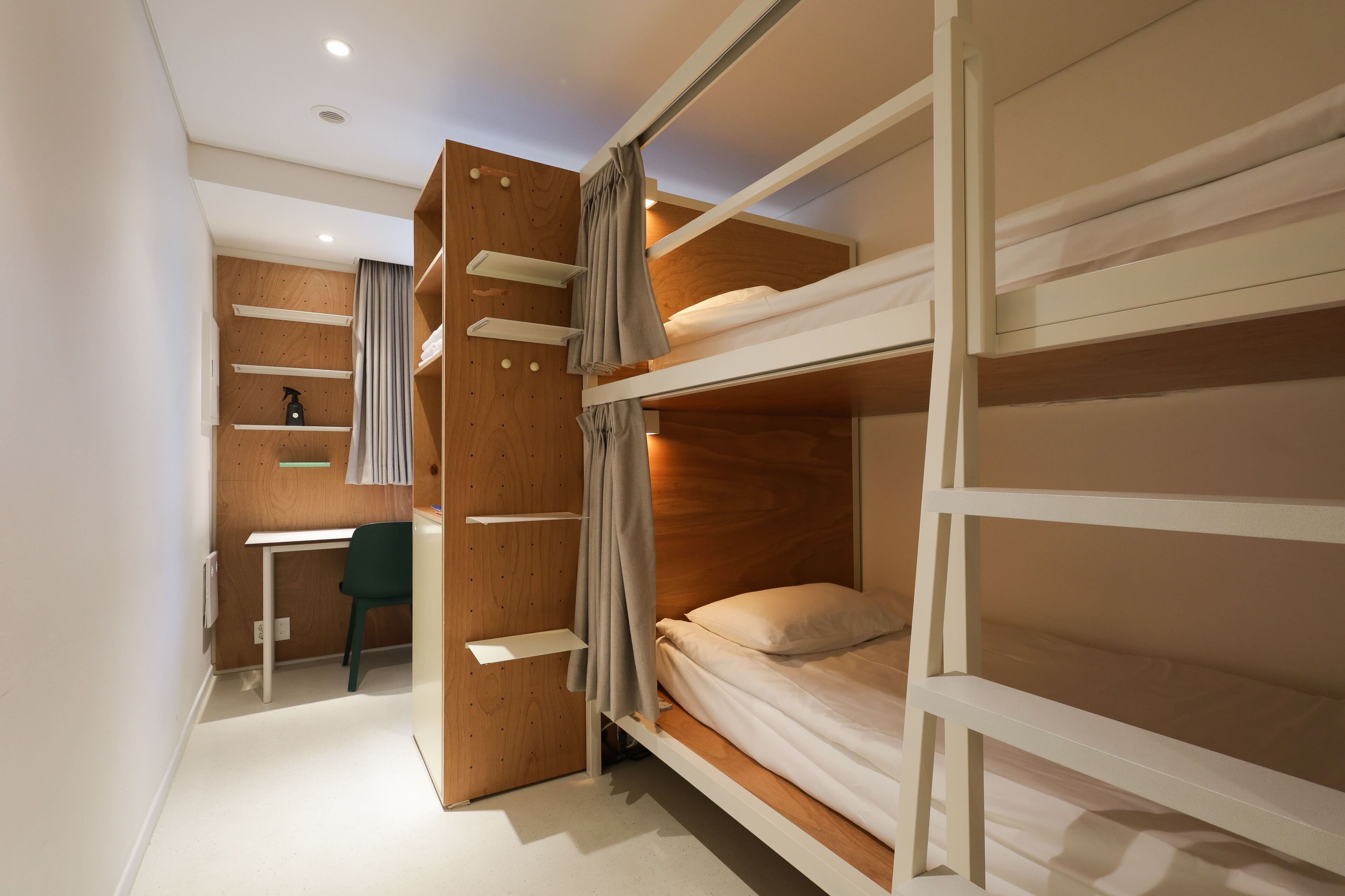 A bunk bed room with a desk and chair, wooden walls, and a curtain.