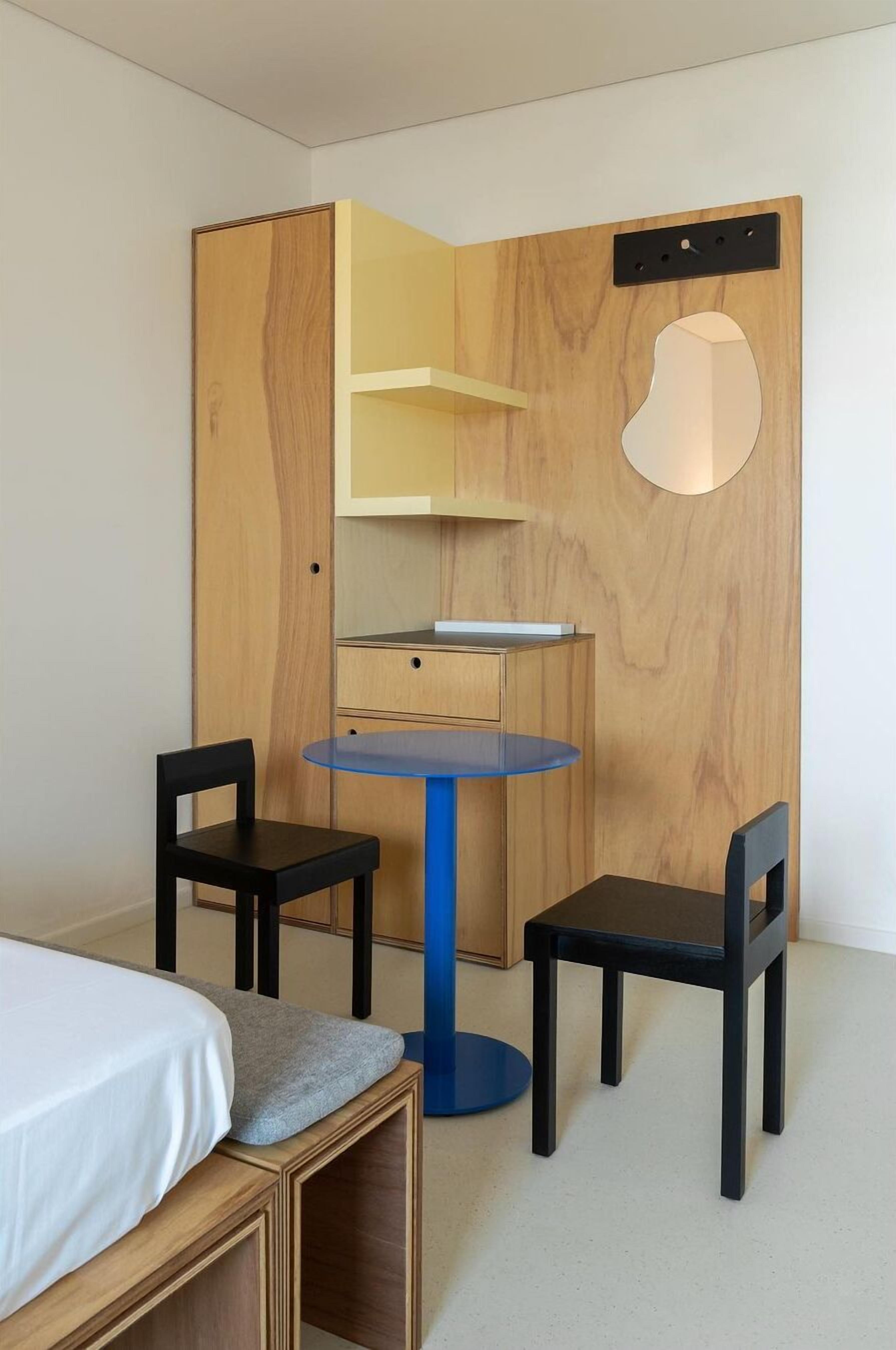 A compact room with a bed, a small round table, two chairs, and a wooden wardrobe with a mirror.