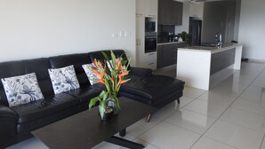 Una sala de estar moderna con un sofá de cuero negro, una mesa de centro con una planta y una cocina al fondo.