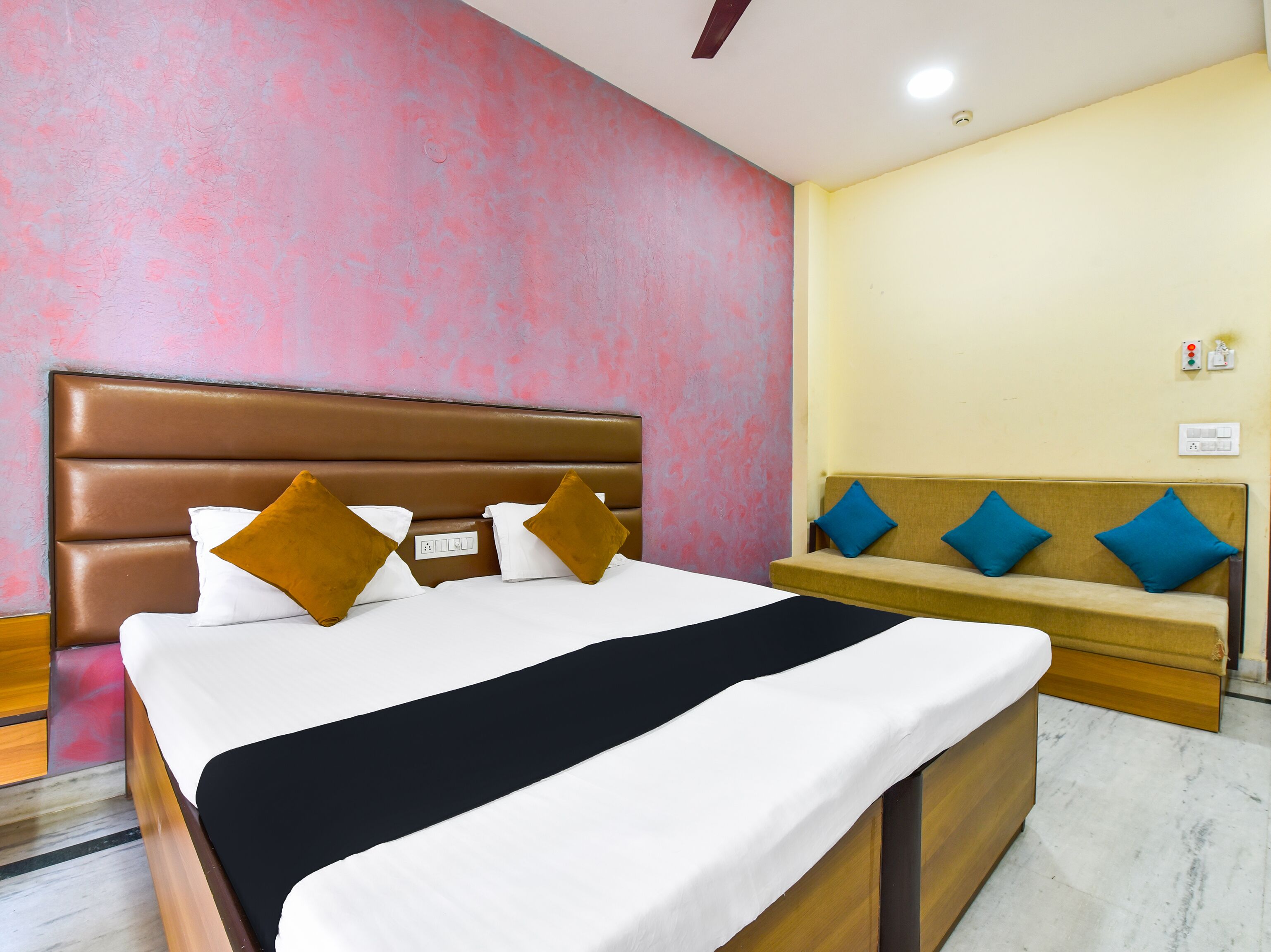 A hotel room with a bed, a bench, and a wall with a pink and yellow color scheme.