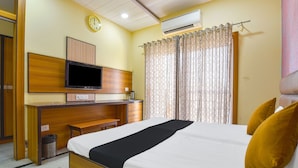 A hotel room with a bed, a desk with a television, a clock, and curtains.