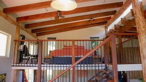 A room with a wooden ceiling, a bed with a red blanket, and a staircase with a railing.
