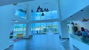 A spacious lobby with large windows, a reception desk, and hanging pendant lights. - Magico Apt 1401 Bello Horizonte (Santa Marta)