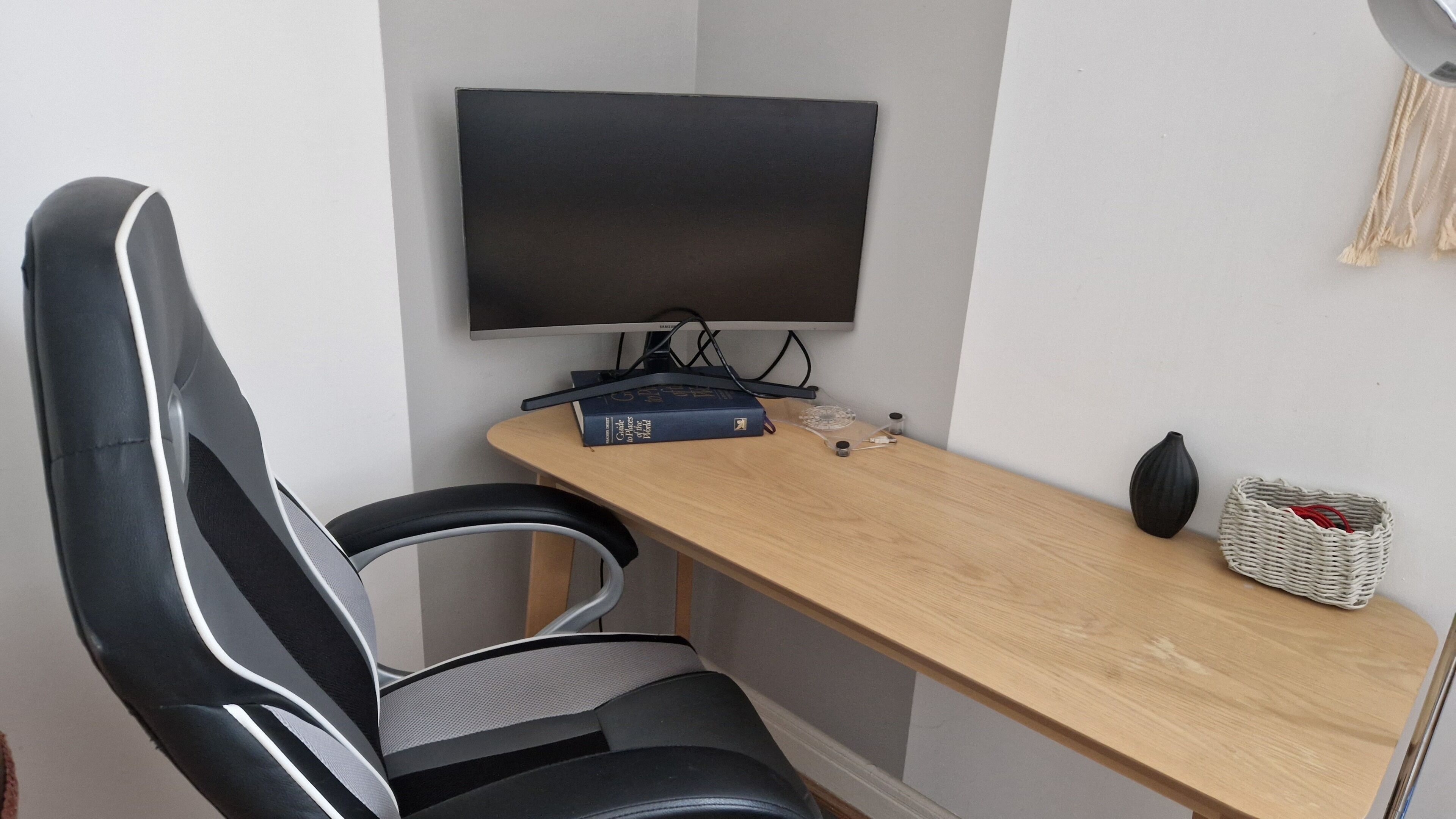 Una silla de oficina moderna, un escritorio con un televisor de pantalla plana, un libro y una cesta decorativa.