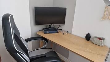Una silla de oficina moderna, un escritorio con un televisor de pantalla plana, un libro y una cesta decorativa.