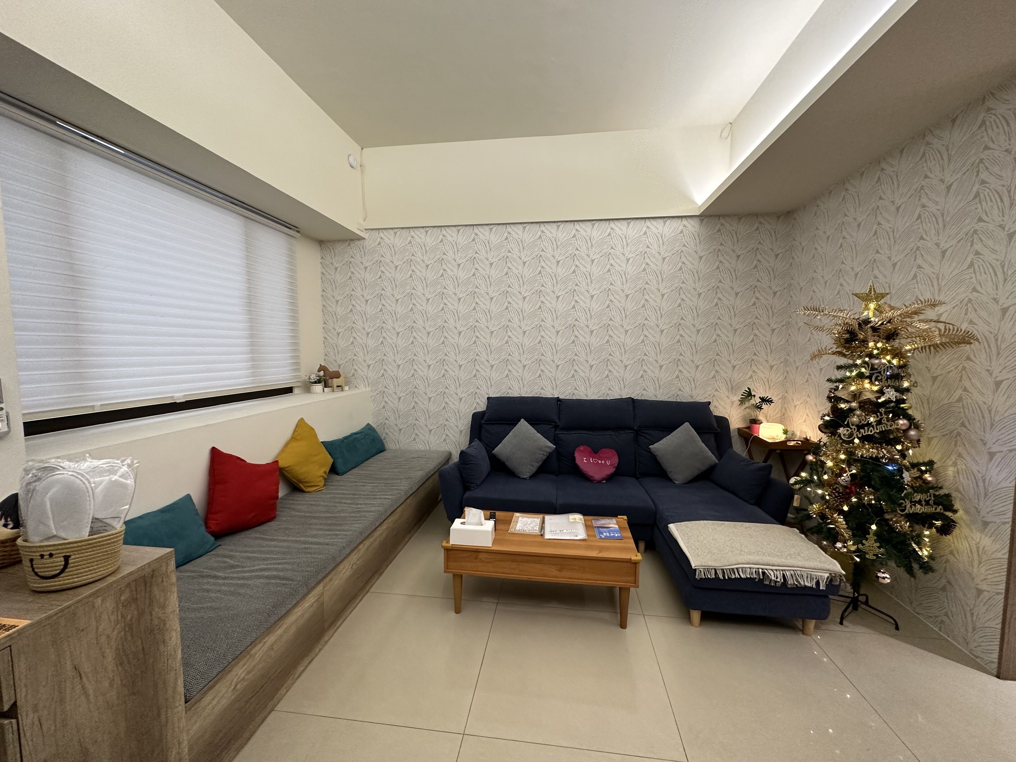 A living room with a sofa, a coffee table, a Christmas tree, and a window with blinds.