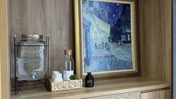 A wooden shelf with a water dispenser, a framed painting, and a reed diffuser.