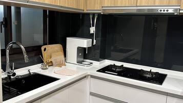 A modern kitchen with white cabinets, a black sink, a built-in stove, and a coffee maker.