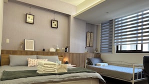 Un dormitorio moderno con una cama de madera, una cama individual y una silla. Hay estantes en la pared con libros y objetos decorativos.