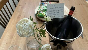 A wooden dining table with a bottle of wine, a flower vase, and a plate with small cups.