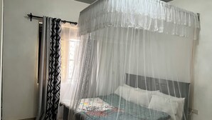 A bedroom with a bed under a mosquito net, a patterned curtain, and a window with a view. - Beautiful Family House (Kampala)