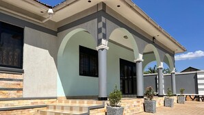 A building with a covered entrance, steps leading up to it, and potted plants. - Beautiful Family House (Kampala)