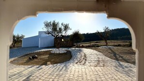 Un patio empedrado con un muro de piedra, un edificio blanco y árboles.