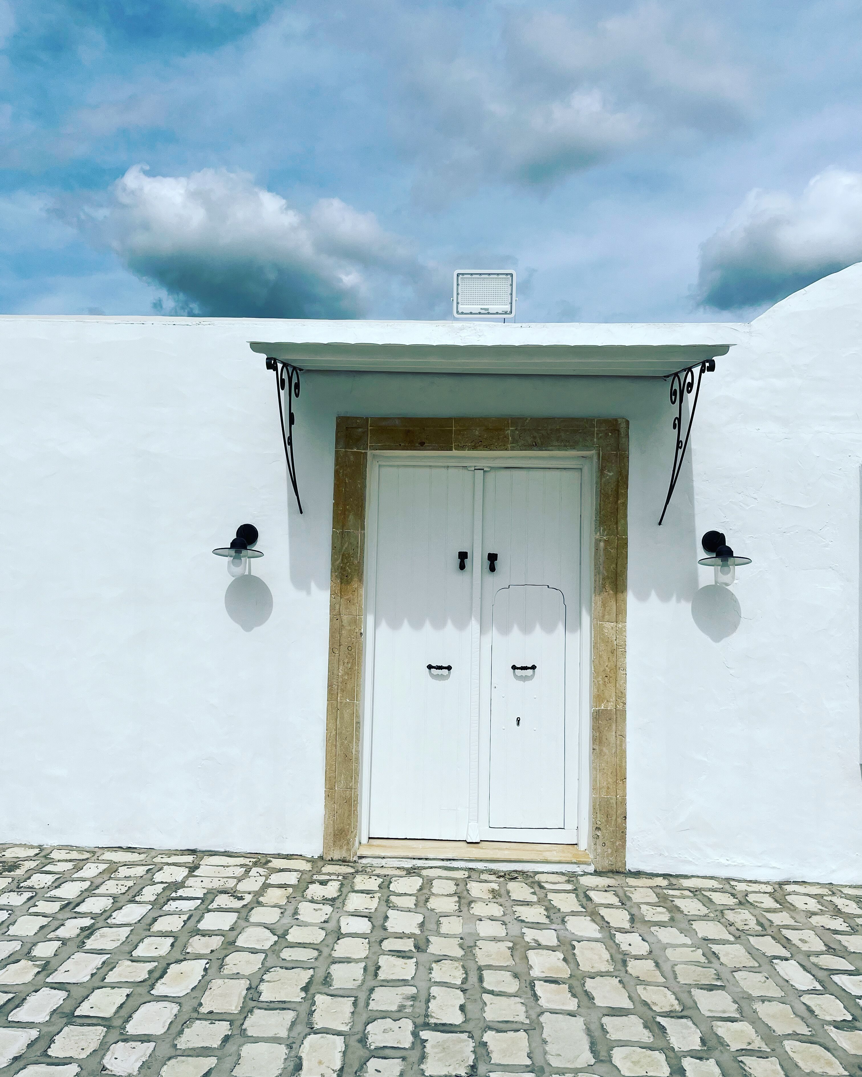 Un edificio blanco con entrada de adoquines y una puerta blanca con dos pomos.