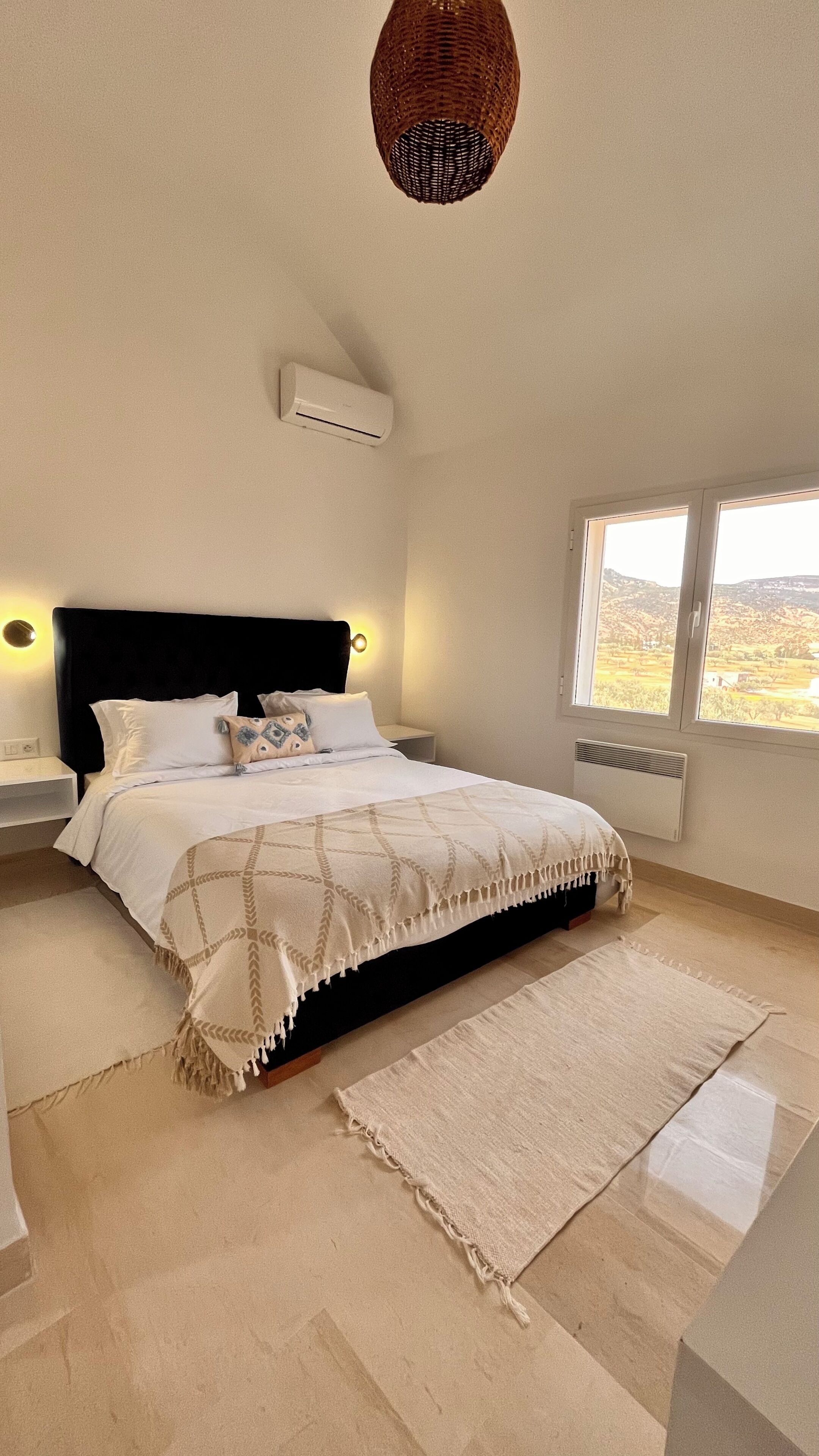 Ein Schlafzimmer mit Bett, Nachttischen, einem Fenster und einer Pendelleuchte.