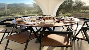 Un comedor con una mesa dispuesta para cuatro personas, rodeada de sillas, y vistas a un paisaje montañoso a través de un ventanal semicircular.