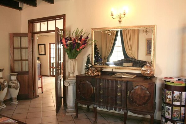 A room with a wooden dresser, a large mirror, and a vase of flowers. - Brooklyn Guesthouses - Stamdard Double Room (Pretoria)