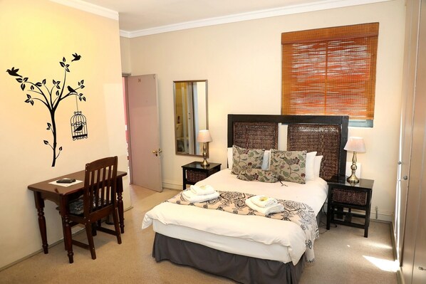 A hotel room with a bed, a desk, a chair, a mirror, and a window with blinds.