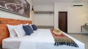 Een net opgemaakt bed met witte beddengoed en blauwe kussens, een groot ingelijst schilderij aan de muur, een hangende hanglamp en een klein tafeltje met een waterkoker.