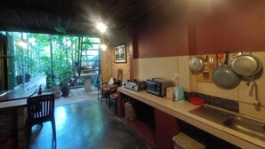 Een kleine keuken met een gasfornuis, een magnetron en een spoelbak. Er staan potplanten en een raam zorgt voor natuurlijk licht.