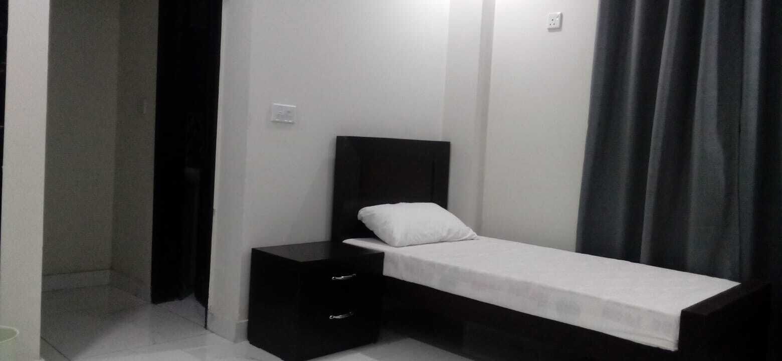 Una camera piccola con un letto singolo, un poggiatesta scuro, un cassetto laterale e un cuscino bianco.