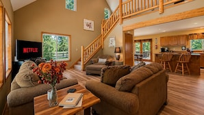A spacious living area with a TV, sofa, and coffee table, a wooden staircase, and a kitchen in the background. - Farmhouse In Plain 2 Bedroom Home by NW Comfy Cabins by RedAwning (Leavenworth)