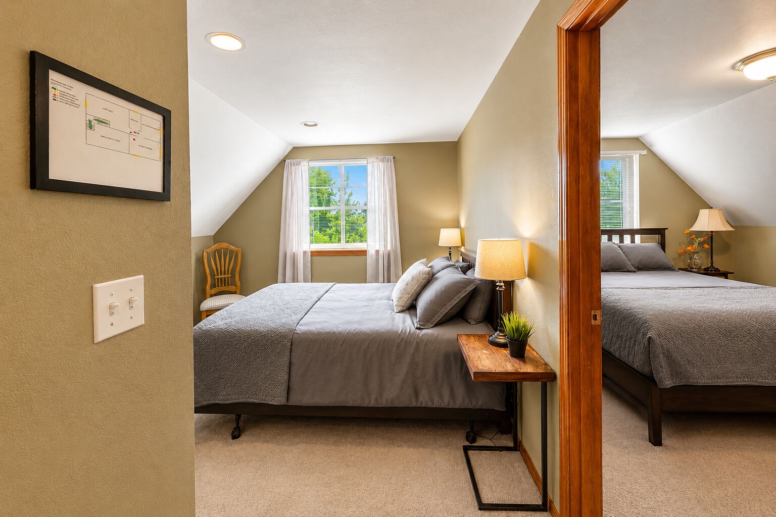 A bedroom with two beds, a wooden nightstand, a lamp, and a framed map on the wall.