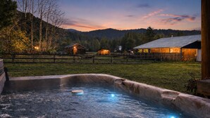 A hot tub in a rustic outdoor setting with wooden cabins in the background. - Farmhouse In Plain 2 Bedroom Home by NW Comfy Cabins by RedAwning (Leavenworth)
