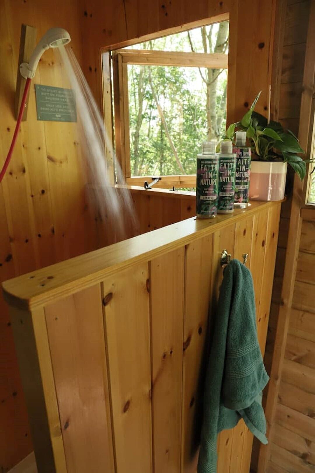 A wooden cabin bathroom with a window, a showerhead, and a towel rack.