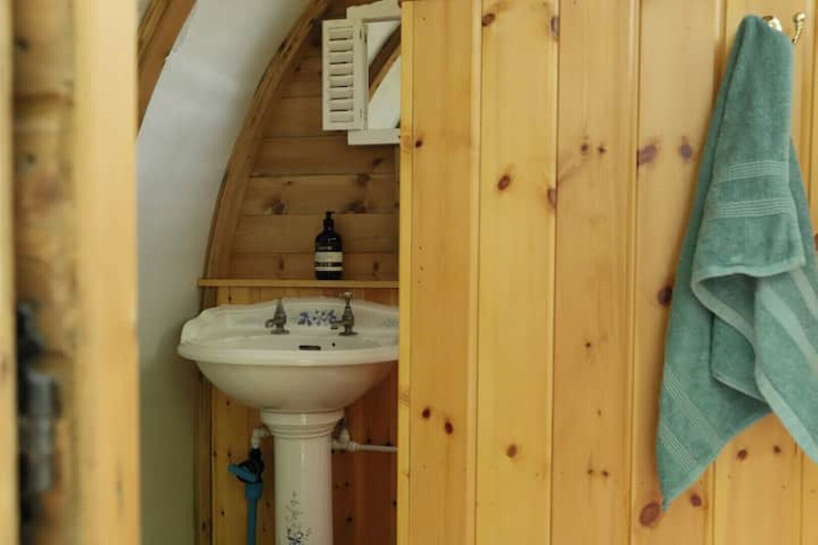 A wooden bathroom with a white sink, a towel hanging on the wall, and a bottle on the shelf.