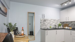 Une cuisine moderne avec des meubles blancs, un plan de travail noir et un pare-feu en carrelage. On y trouve un coin repas avec une table et des chaises en bois, un vase avec des fleurs et une bouteille de vin.