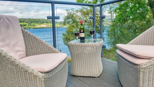 Un balcon agrémenté de meubles en osier et d’une table en verre sur laquelle sont disposées des bouteilles de vin et des verres.