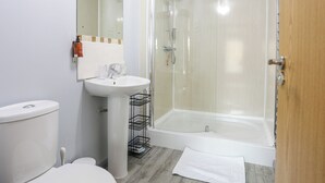 Une salle de bain comprenant des toilettes, un lavabo et une douche fermée par une paroi de verre.