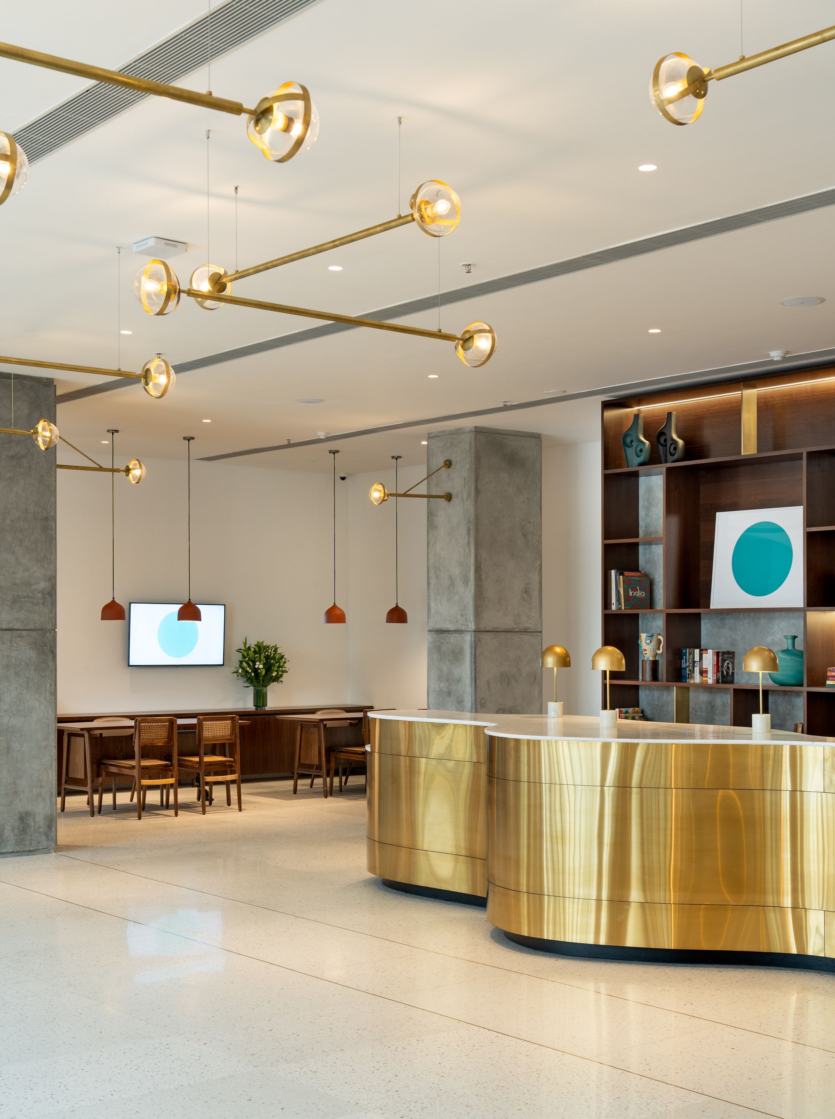 Un área de recepción moderna con un mostrador curvo dorado, sillas de madera e iluminación colgante.