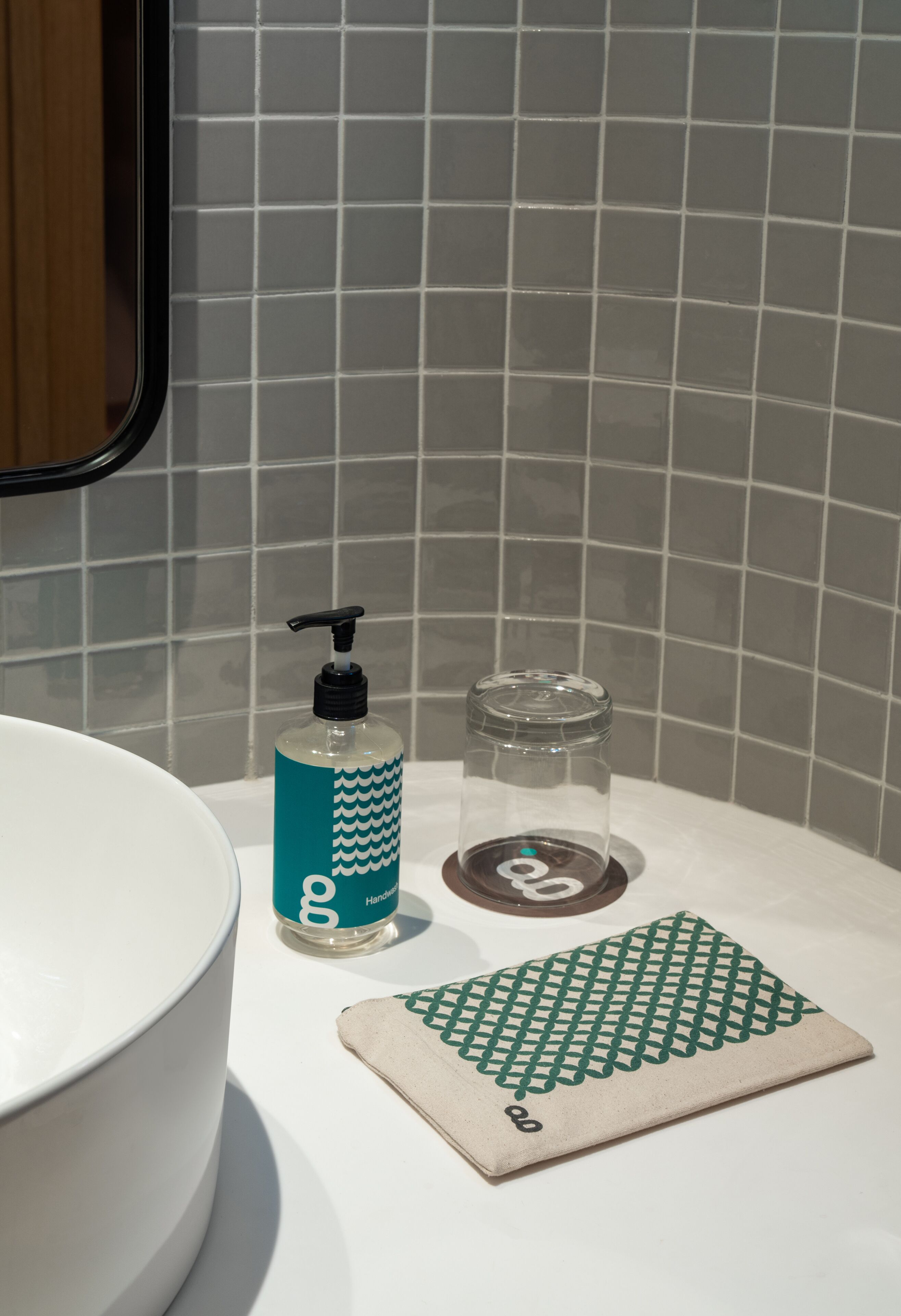 Ein Badezimmer mit einem weißen Waschbecken, einem türkisfarbenen Seifenspender, einer klaren Glasflasche und einem gemusterten Handtuch auf der Ablagefläche.