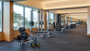A gym with weightlifting equipment, cardio machines, and large windows offering a view of the outdoors. - Greenpark Bengaluru (Bengaluru)