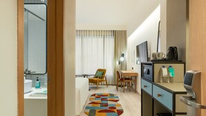 A modern hotel room with a wooden ceiling, a kitchenette, a dining area with a table and chairs, and a bathroom visible through an open door. - Greenpark Bengaluru (Bengaluru)