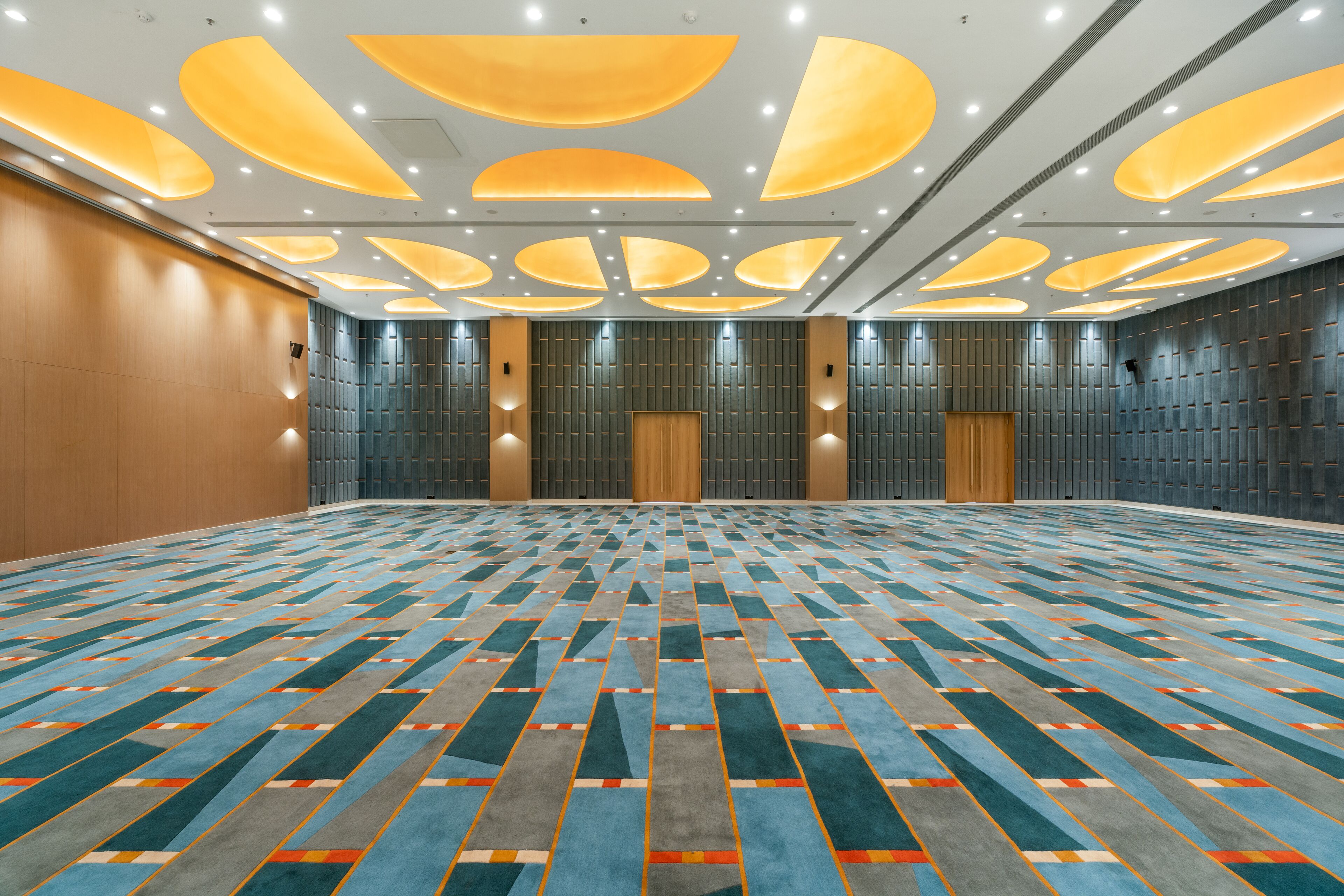 A spacious conference room with a patterned carpet, recessed lighting, and a wooden panel wall.