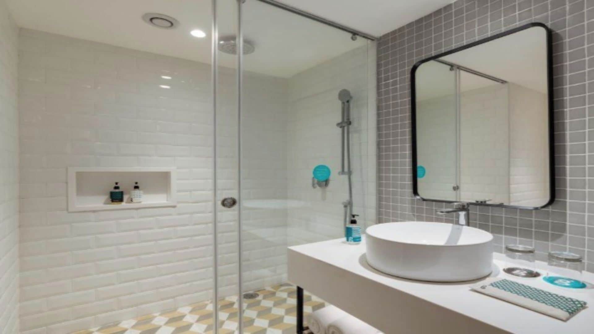 A modern bathroom with a glass shower enclosure, a white sink with a round basin, and a mirror with a black frame.