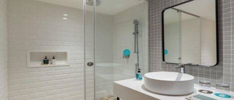 A modern bathroom with a glass shower enclosure, a white sink with a round basin, and a mirror with a black frame.