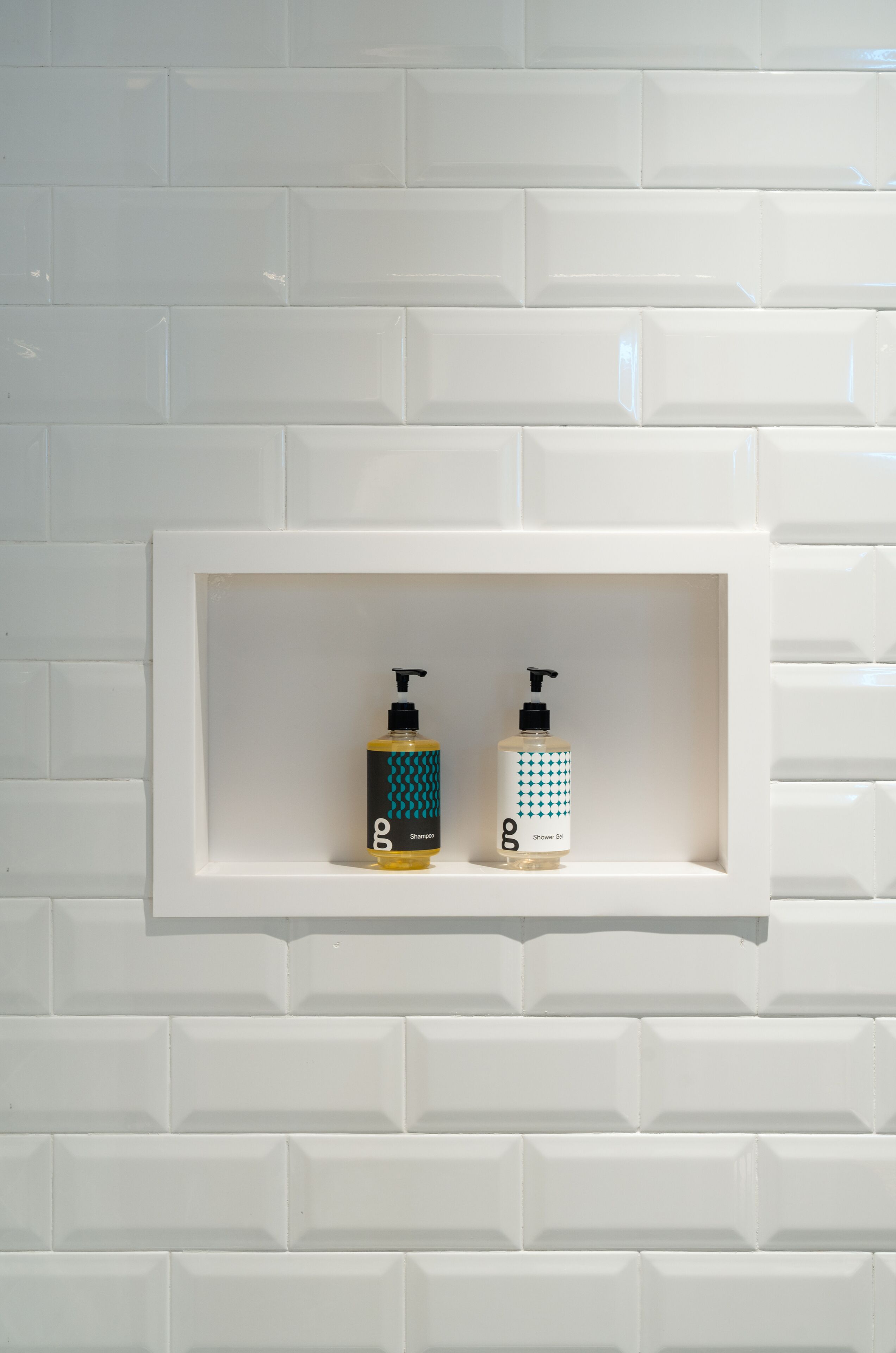Ein Badezimmer mit weiß gefliester Wand und einer Ablage mit zwei Shampoo- und Duschgelflaschen.