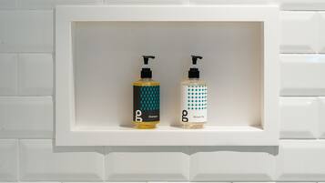 Une salle de bain avec un mur recouvert de carreaux blancs et une étagère contenant deux bouteilles de shampoing et de gel douche.