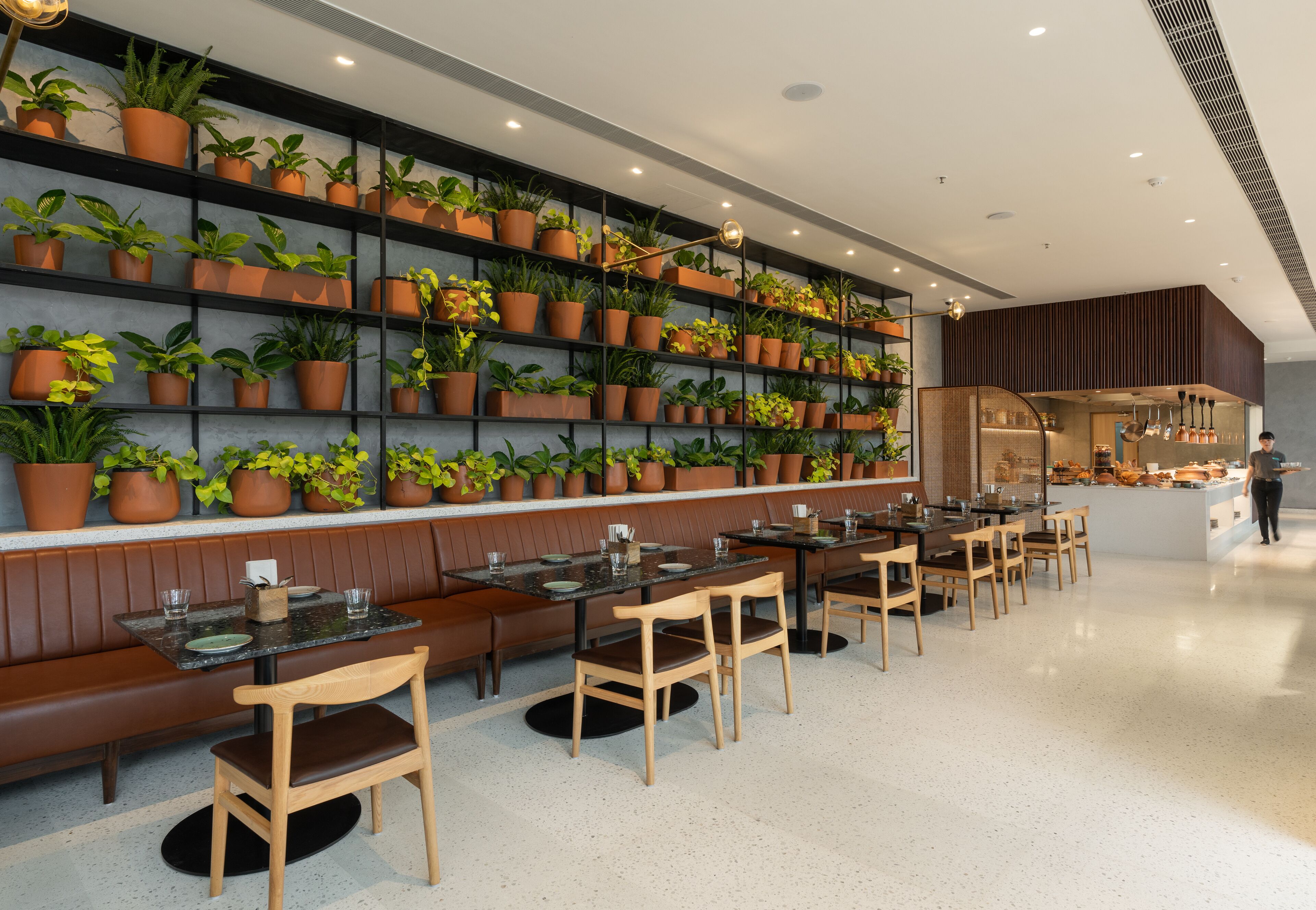 Un ristorante moderno con diversi tavoli e sedie, un'ampia area con panche e una parete decorata con piante in vaso.