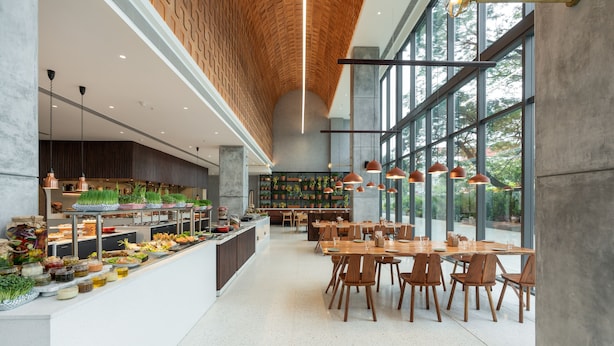 A spacious dining area with a long counter displaying various food items, surrounded by wooden tables and chairs. - Greenpark Bengaluru (Bengaluru)